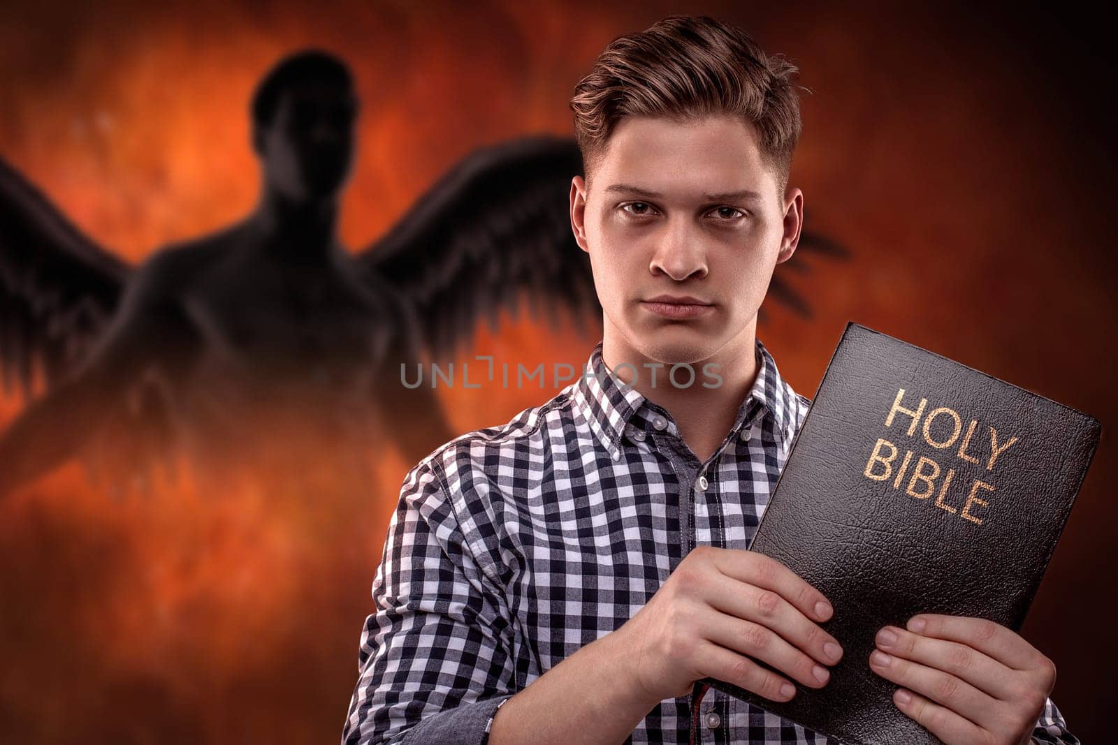Young christian man holding a Bible with a devil in background (concept against temptation by God's Word)