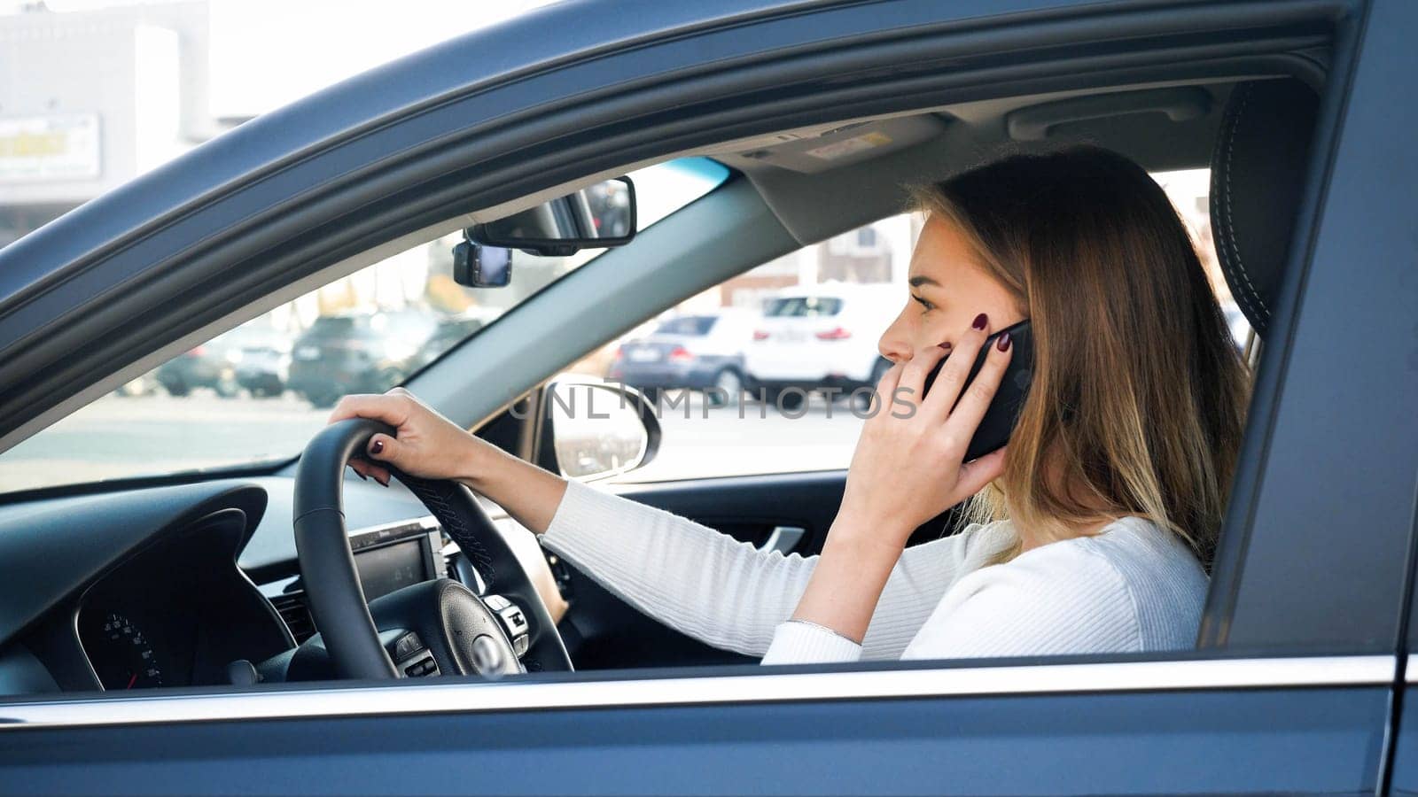 Portrait of young businesswoman using smartphone while driving a car. Driver may be distrated that may cause car accident.