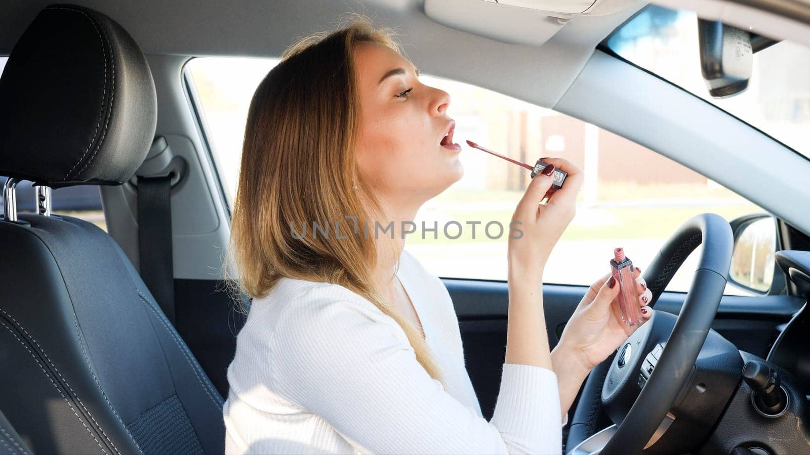 Portrait of beautiful young woman using car mirror twhile applying lipstick.