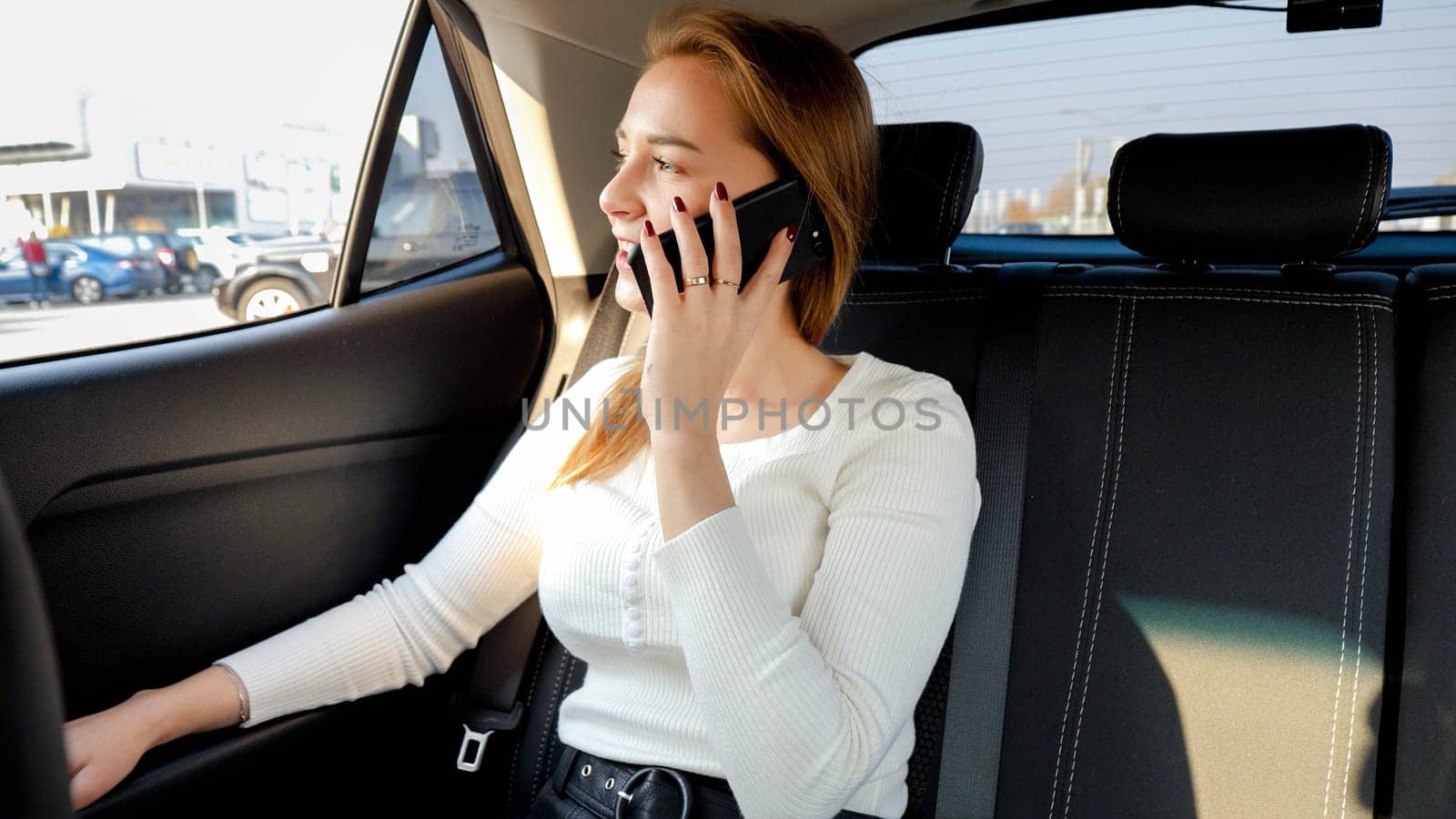 Beautiful businesswoman talking by smartphone and looking out of the car window while riding to work at morning.