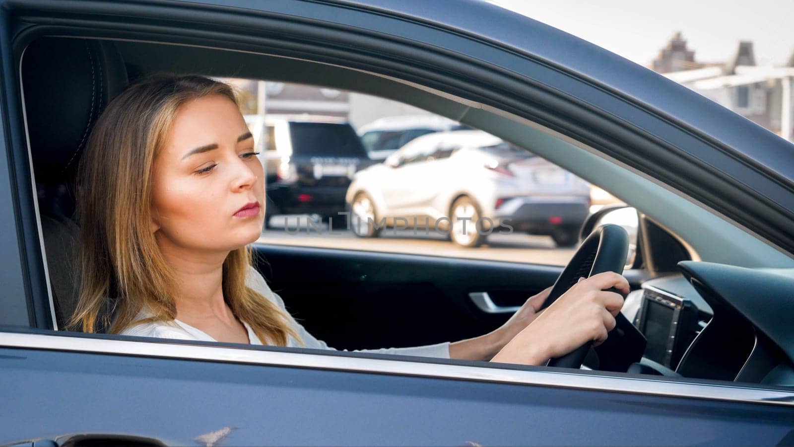 Portrait of female driver looking out of the open window while driving a car in city.