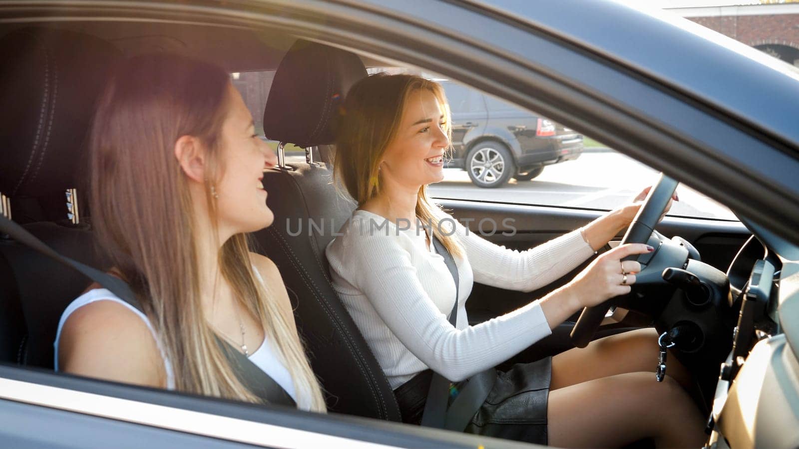 Portrait of two girls talking and smiling while driving in car with open windows.