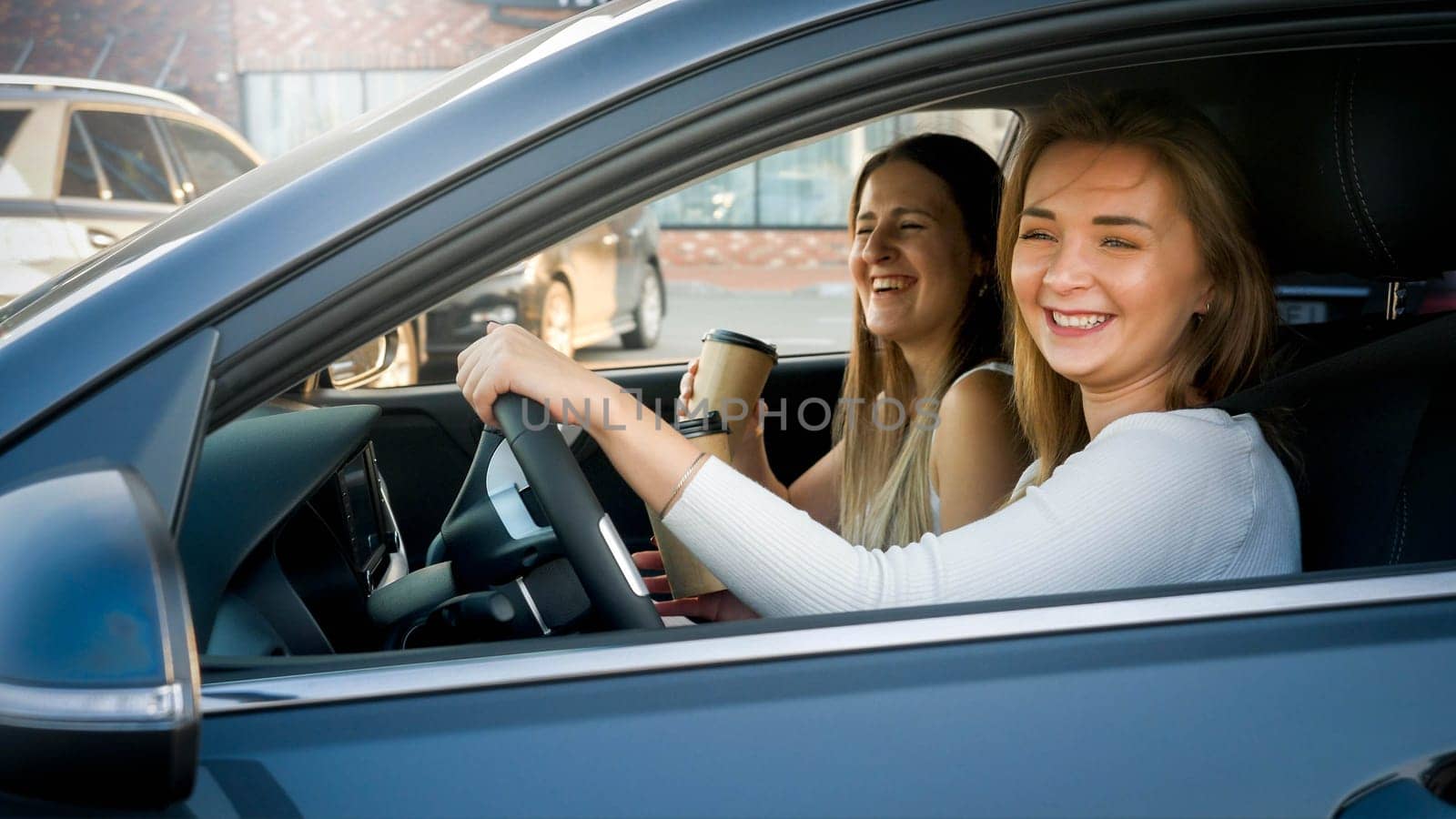 Portrait of happy laughing girls having fun while driving a car in city.