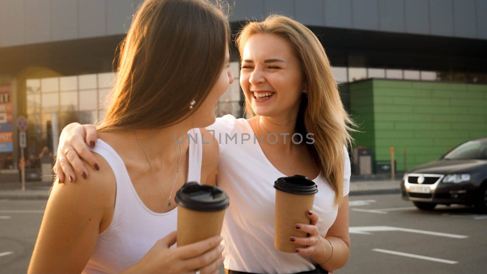 Happy smiling girls drinking coffee while walking on shopping mall car parking.