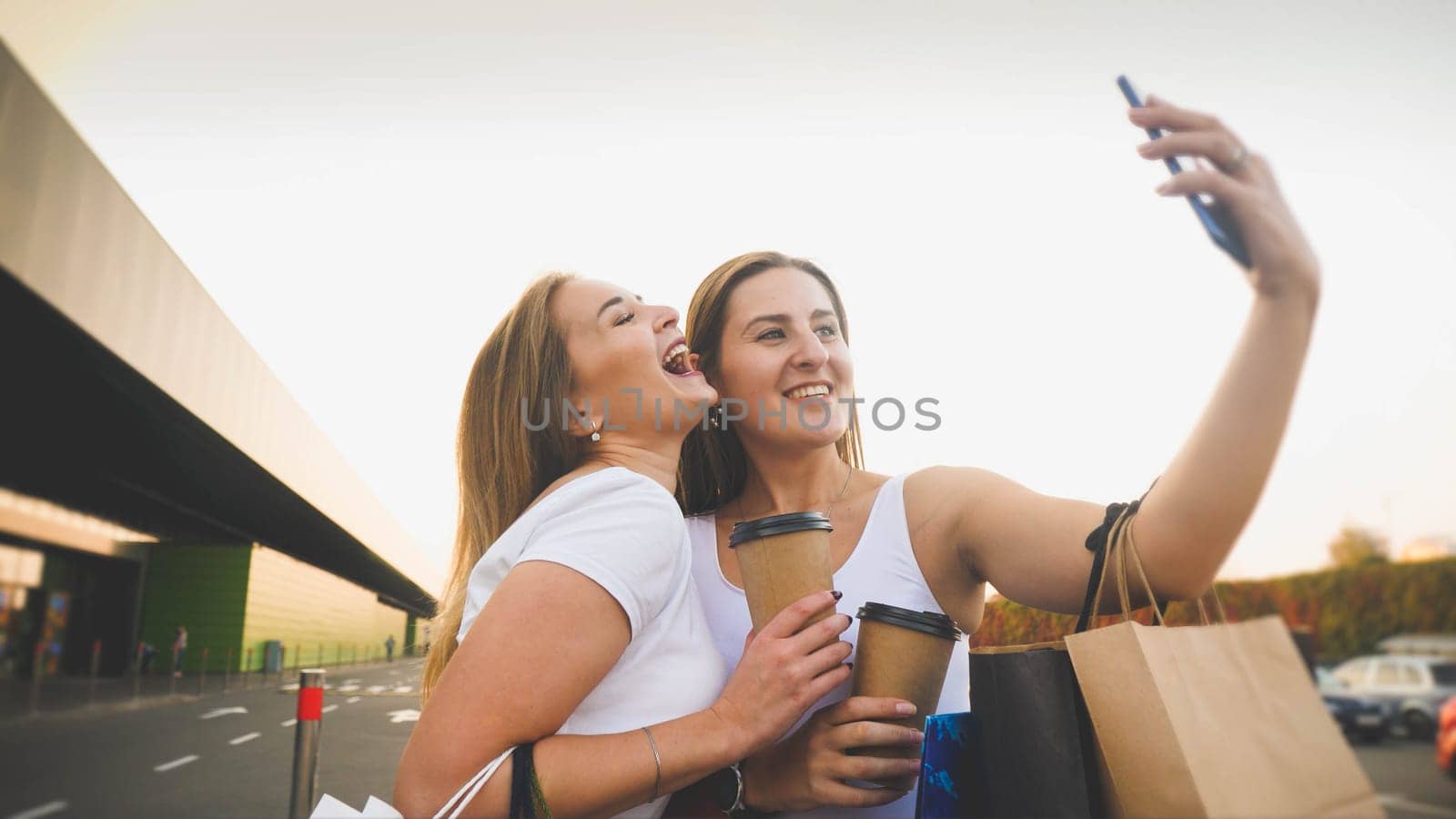 Toned portrait of two girl friends making selfie photo on smartphone at big shopping mall.