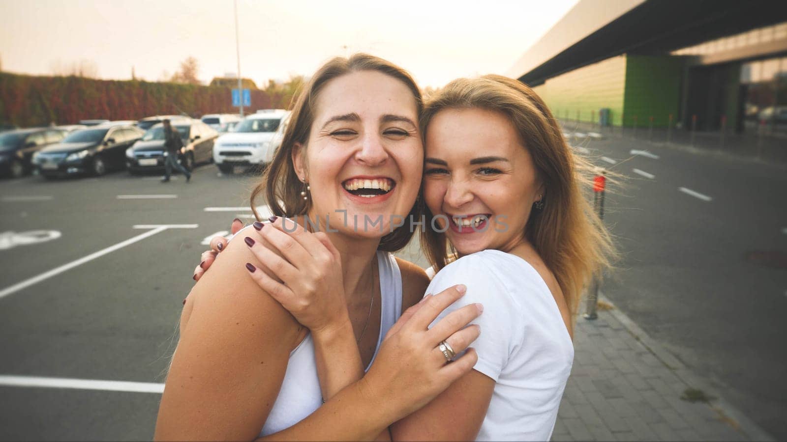 Toned portrait of two smiling and laughing girls friends hugging on car parking at shopping mall.