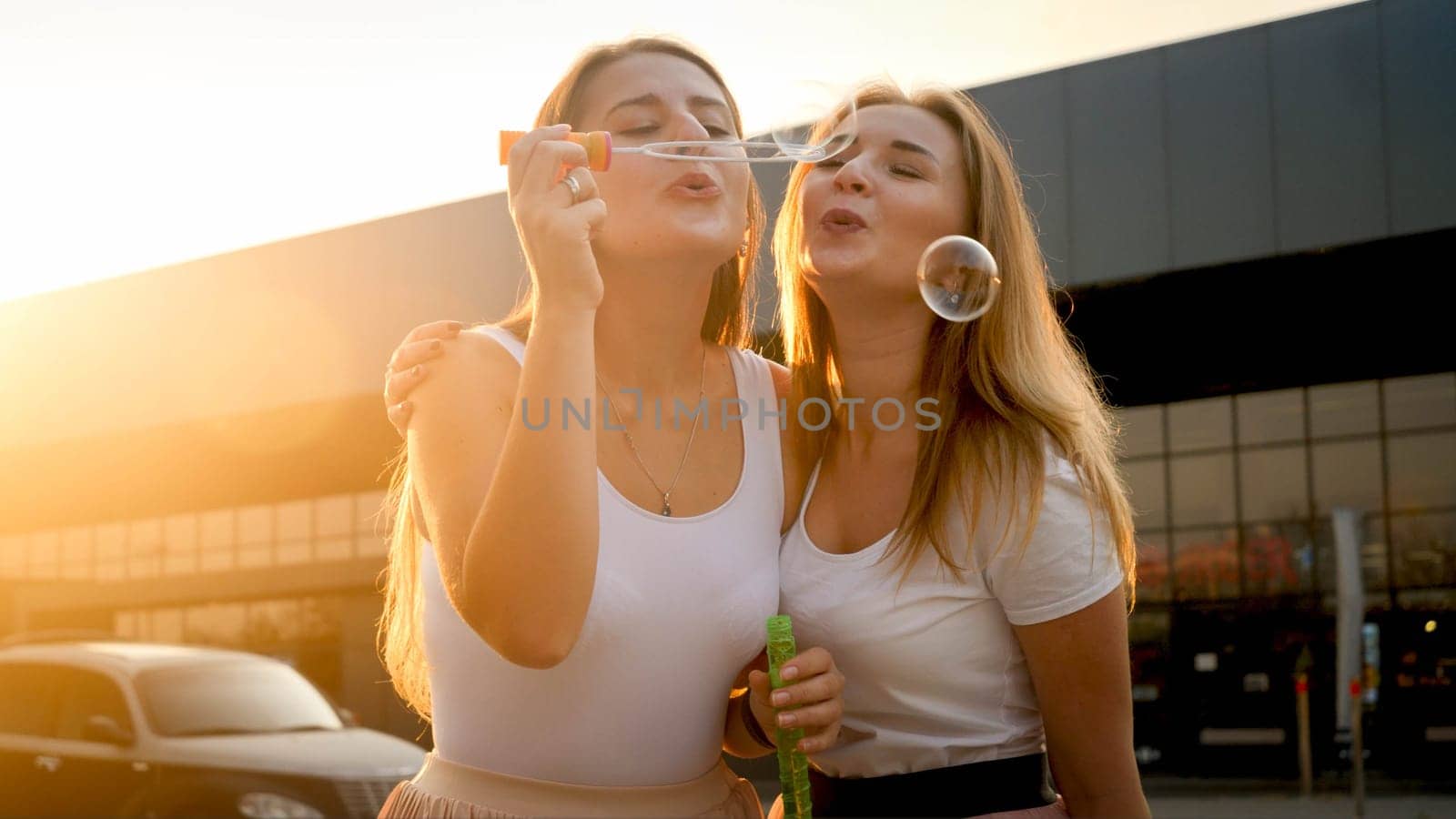 Two young smiling women blowing soap bubbles and laughing.