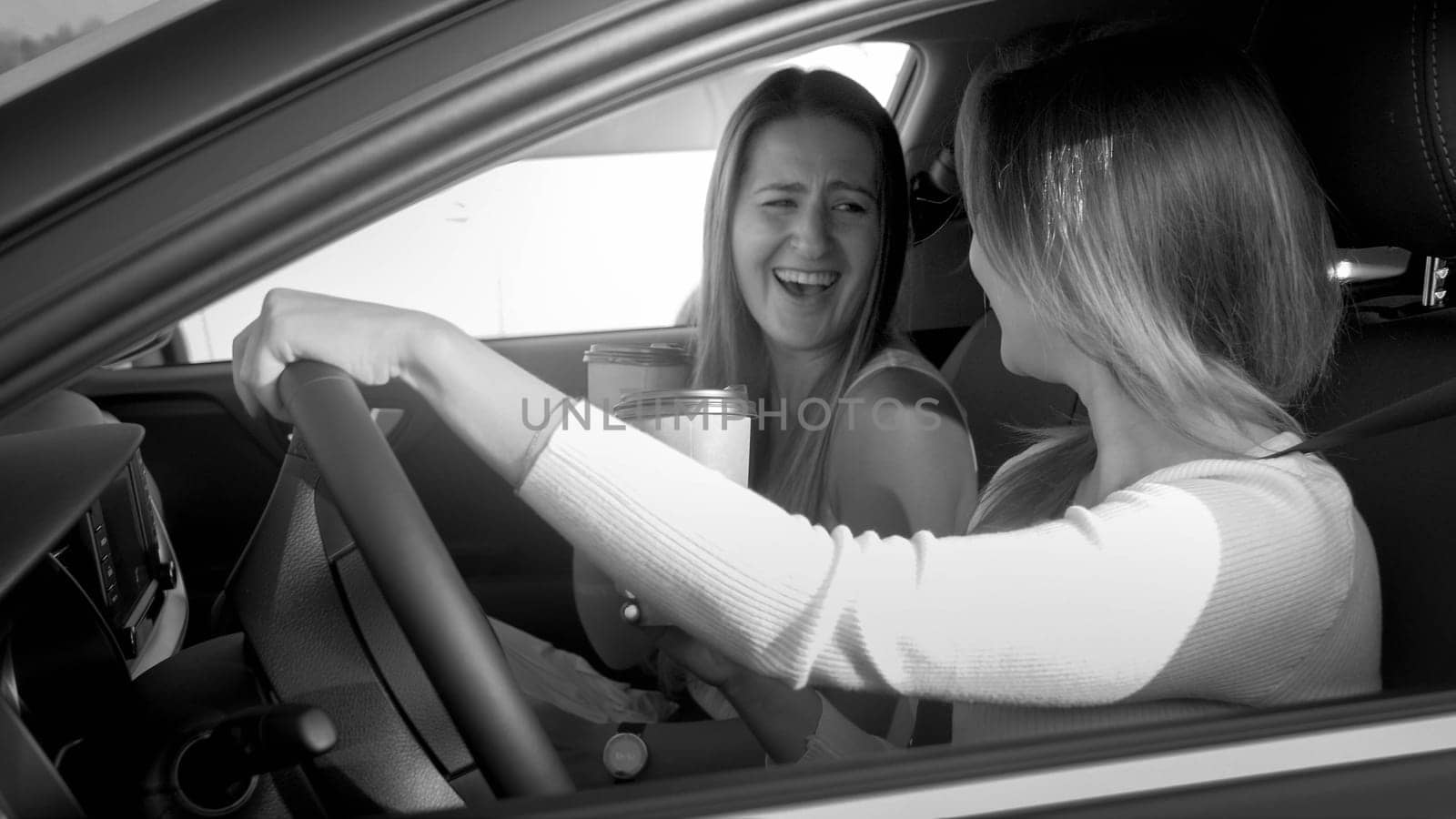 Black and white portrait of two laughing girls singing and smiling hile driving a car.