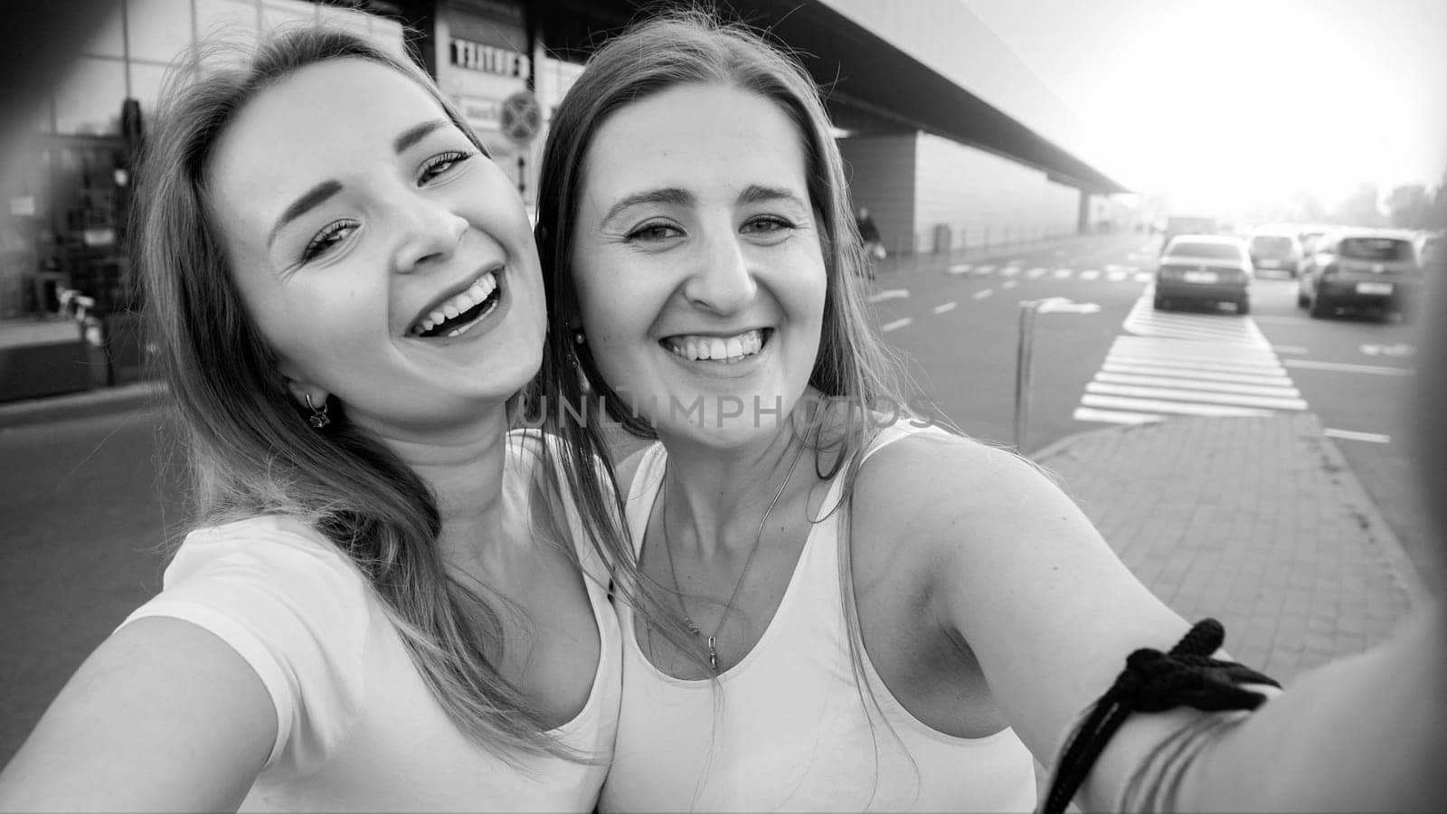 Black and white portrait of happy laughing female friends making selfie at shopping mall entrance.