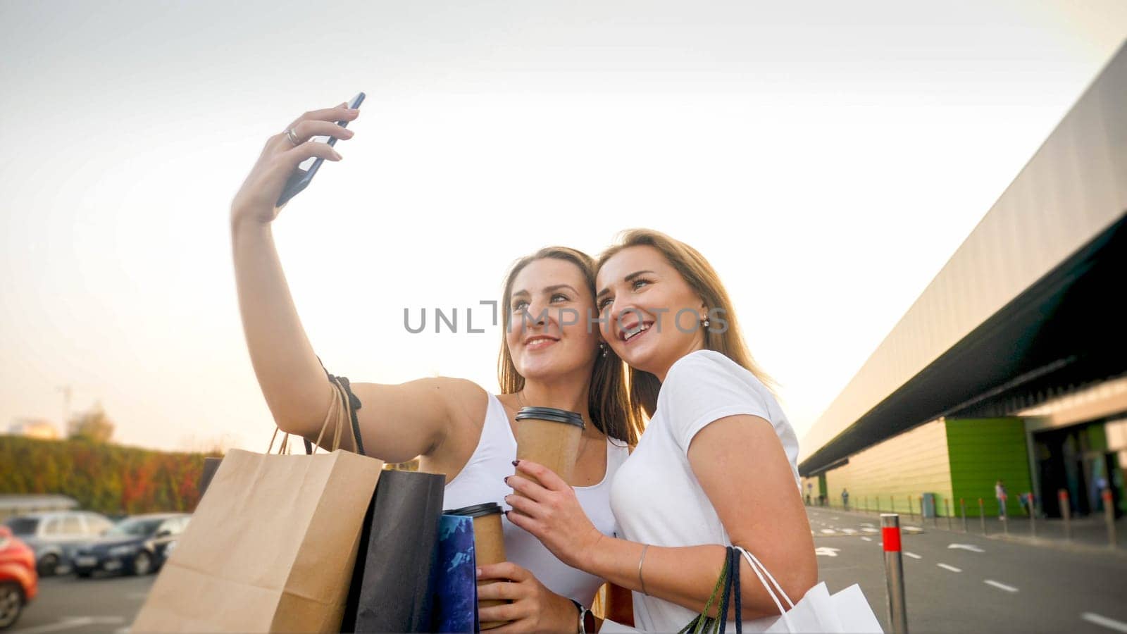 Portrait of two female friends making selfie photo of on smart phone after making shopping at mall.