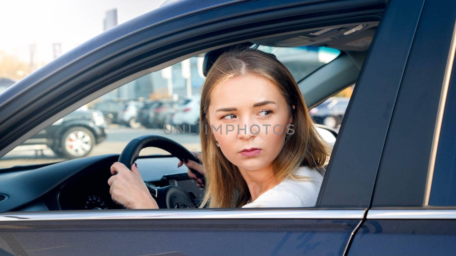 Portrait of young blonde woman looking for the parking place while driving a car.