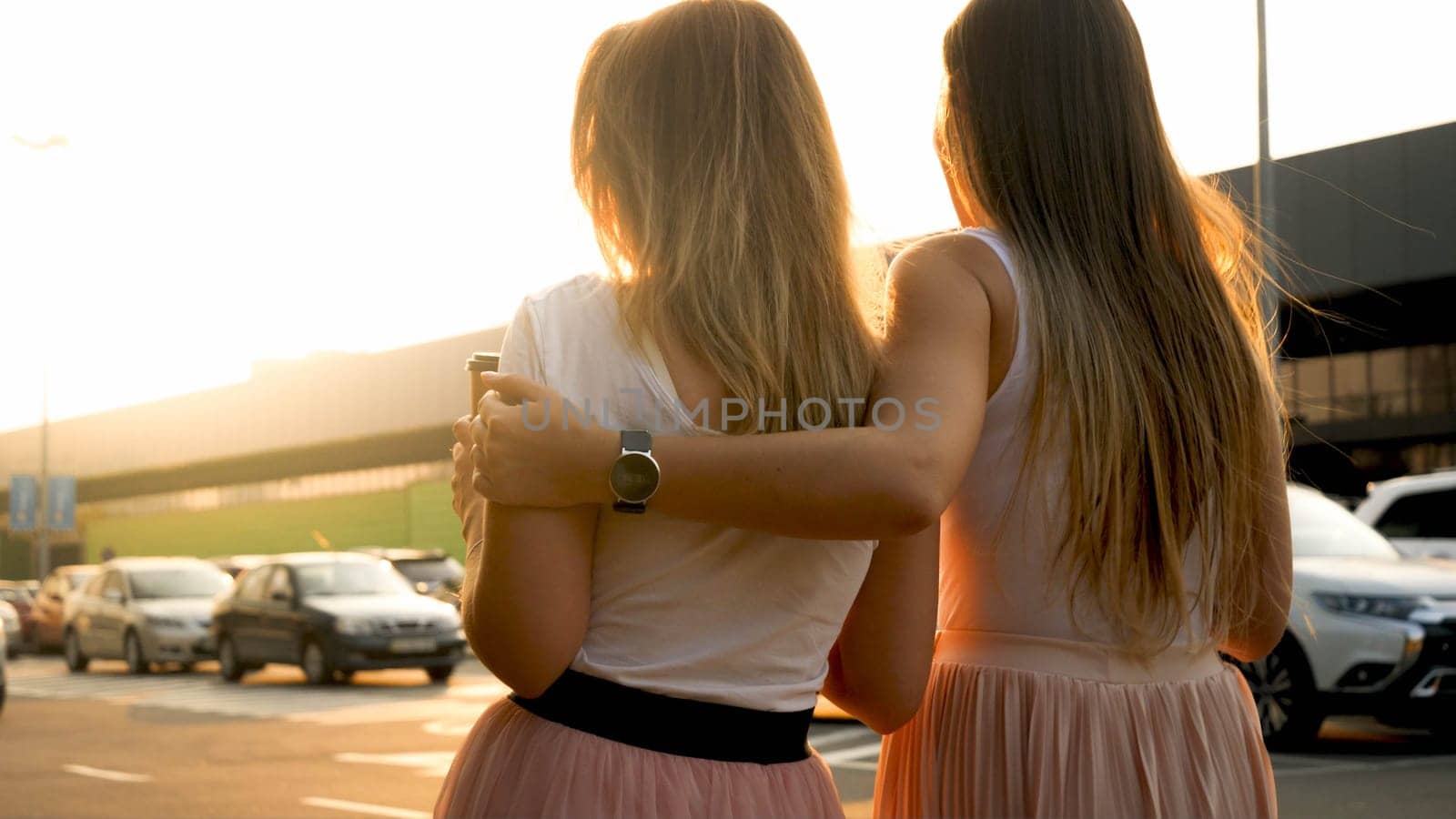 SIlhouette of two hugging girl friends walking on city street at sunset.
