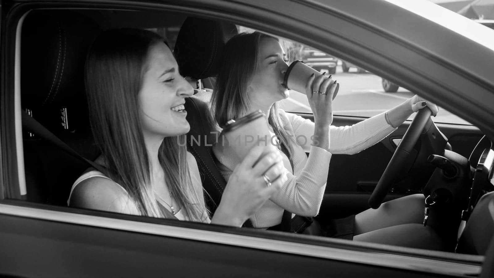 Portrait of beautiful female driver drinking coffee while driving a car with her girl friend.