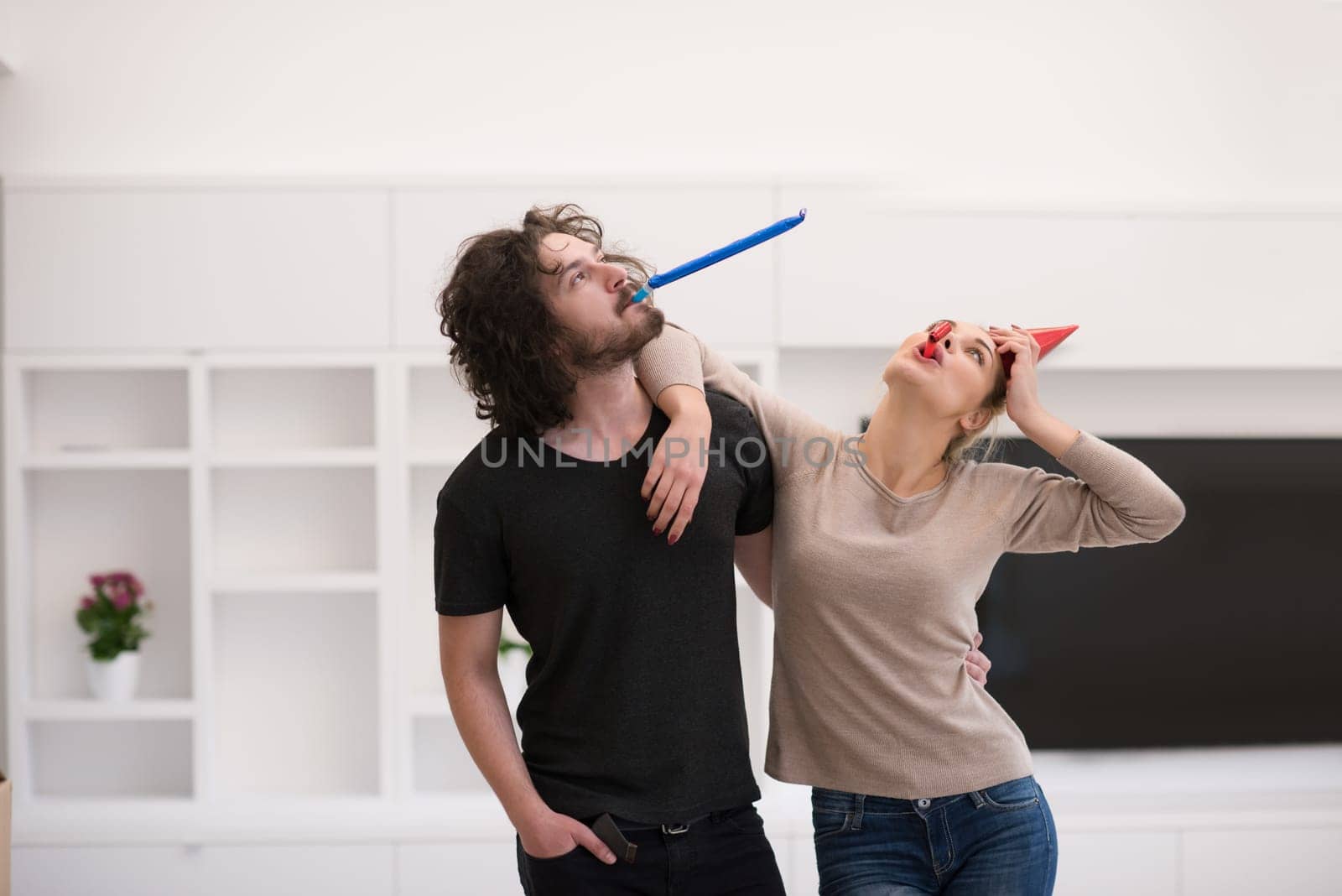 Young happy couple in party hats blowing in whistle isolated on a white background