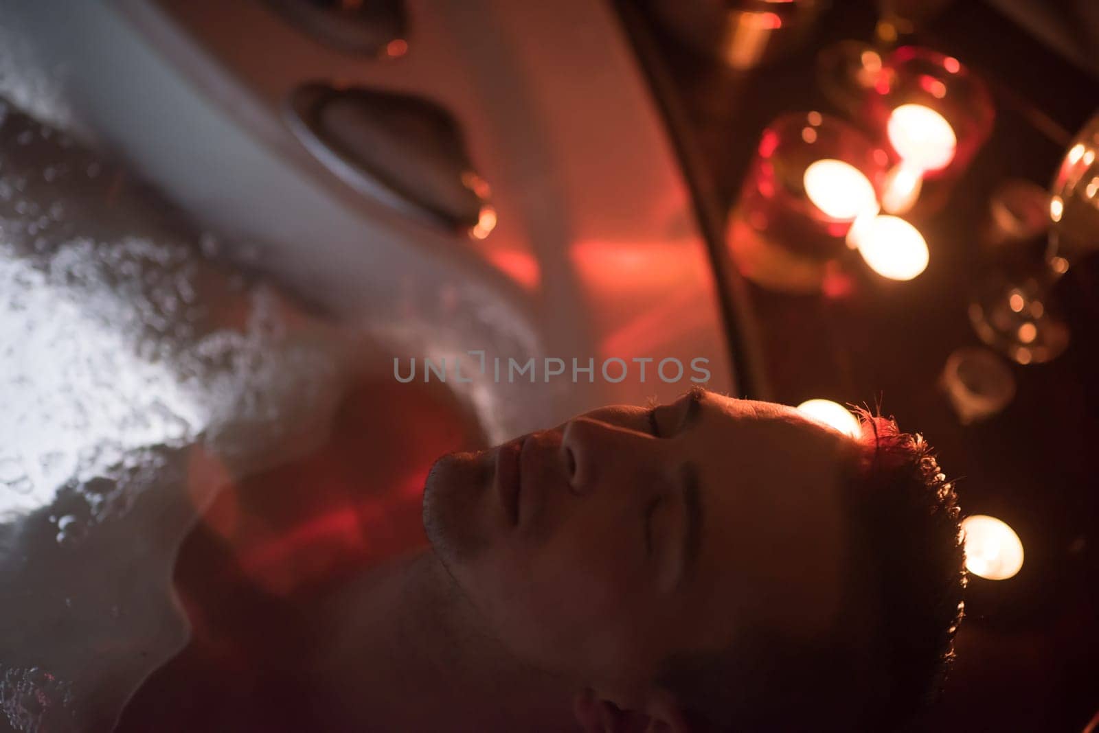 young handsome man enjoys relaxing in the jacuzzi with candles and champagne at luxury resort spa