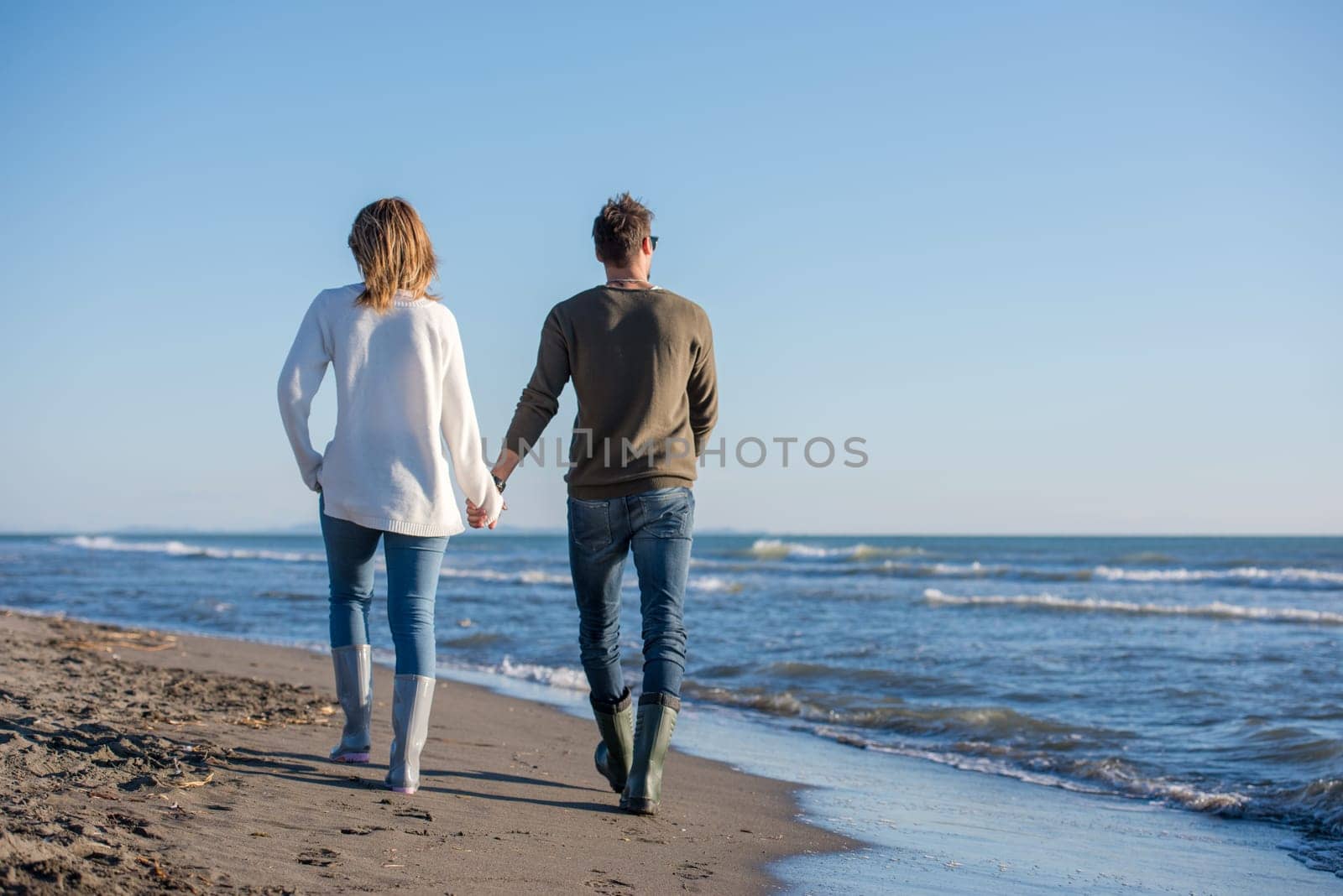 Young couple having fun walking and hugging on beach during autumn sunny day