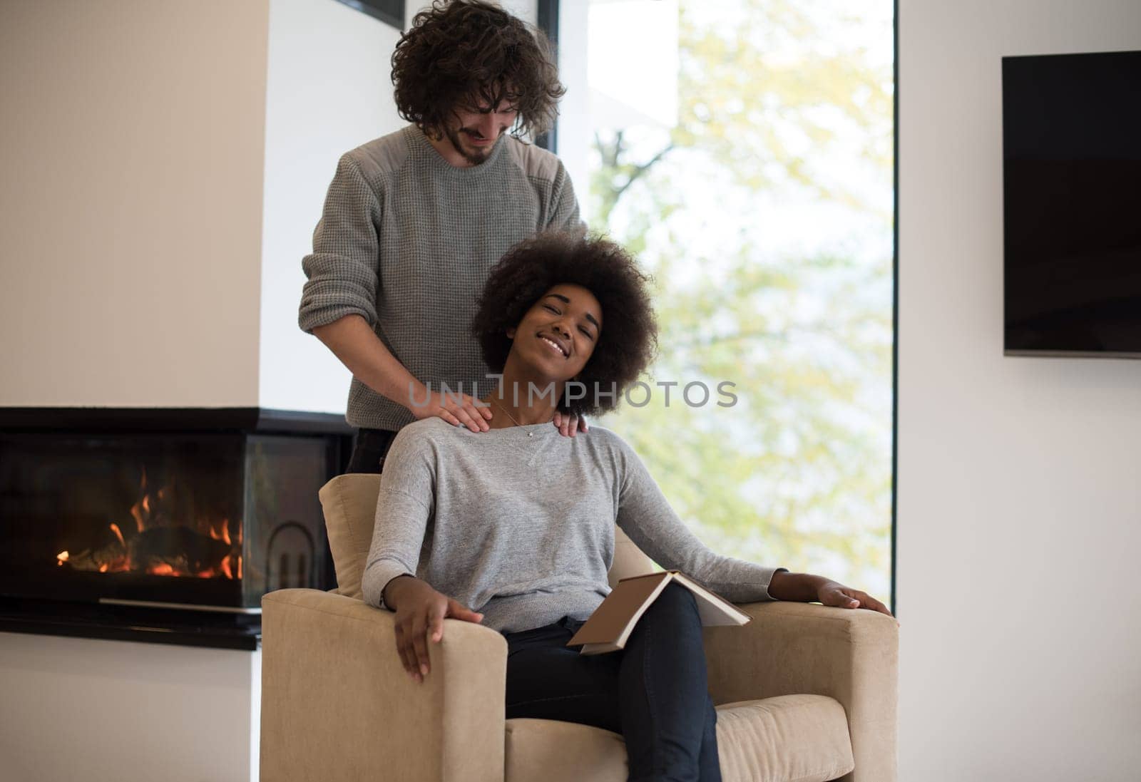 Young beautiful multiethnic couple hugging in front of fireplace at home when reading a book at autumn day