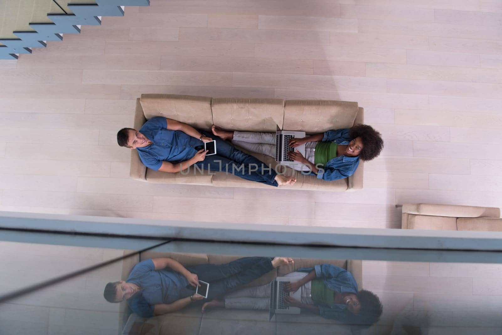 Young multiethnic couple relaxes in the luxury living room, using a tablet and laptop computer top view