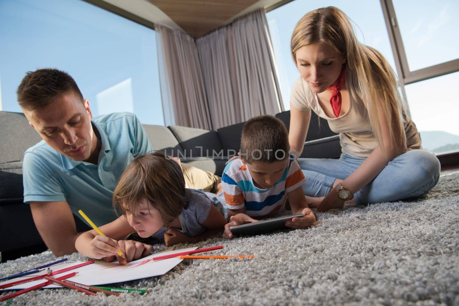 Happy Young Family Playing Together at home on the floor using a tablet and a children's drawing set