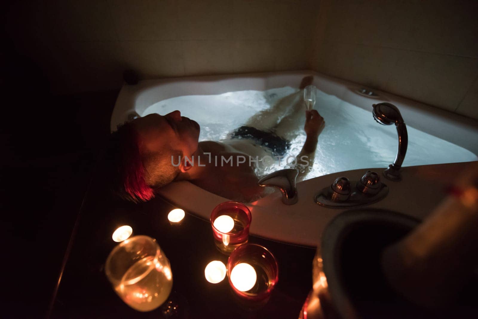 young handsome man enjoys relaxing in the jacuzzi with candles and champagne at luxury resort spa