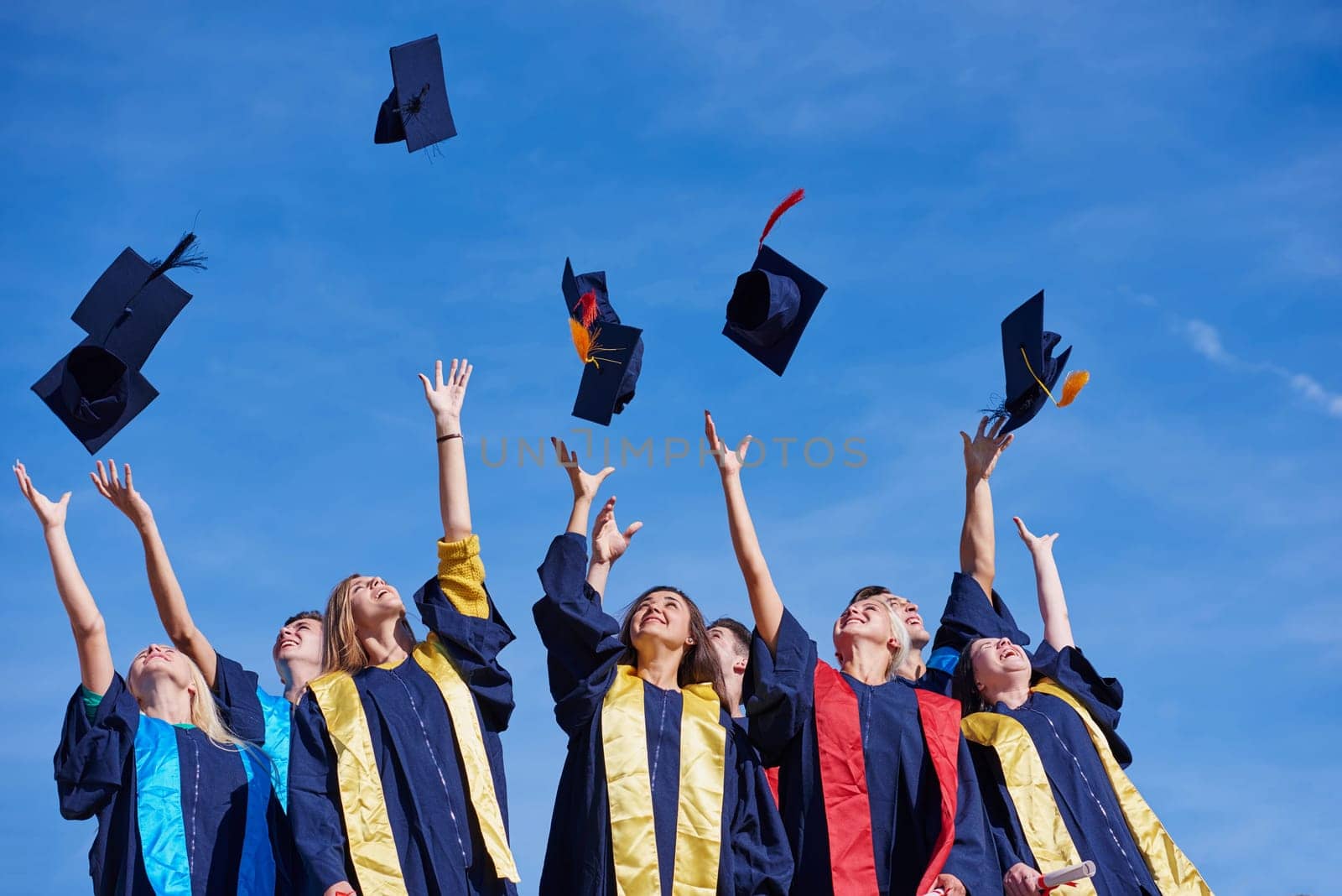 high school students graduates tossing up hats over blue sky.