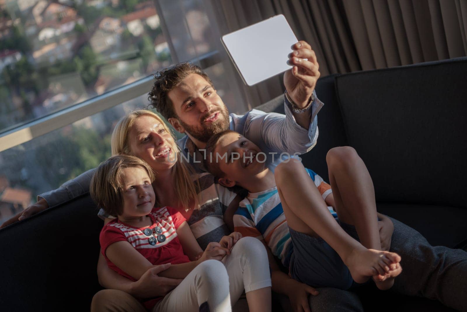 happy couple spending time with kids using tablet computer on sofa at home