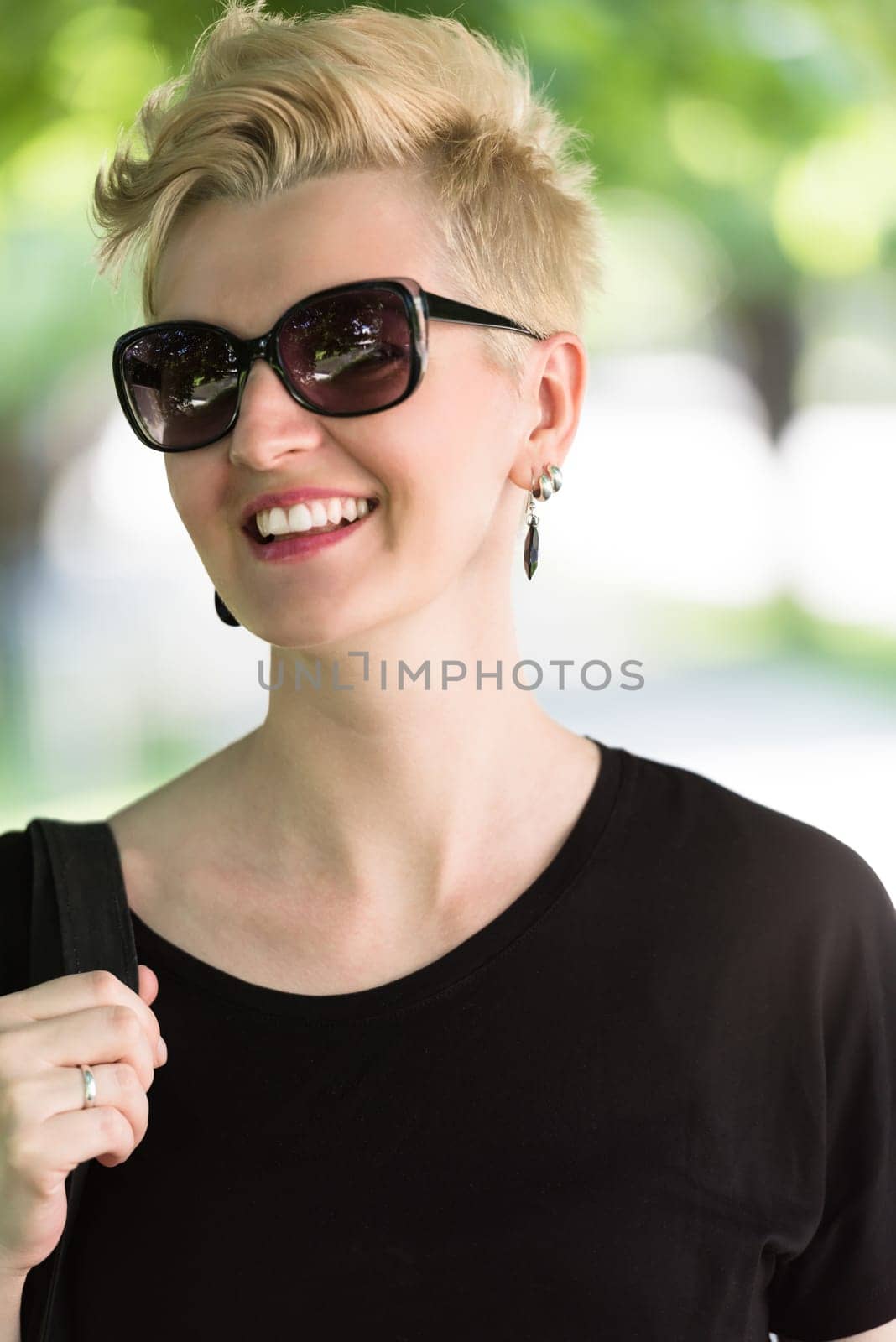 Beautiful fashionable young woman with short blond hair and sunglasses posing in the park