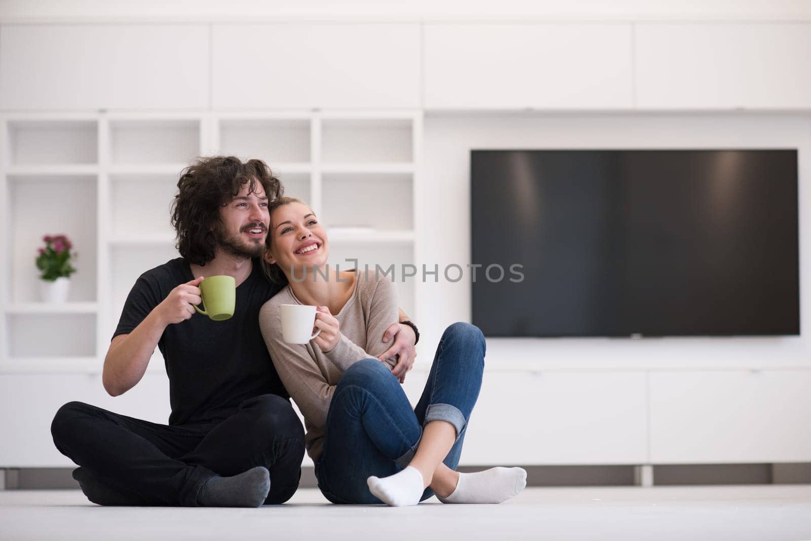 portrait of young happy beautiful couple sitting on the floor and drinking coffee in their new home