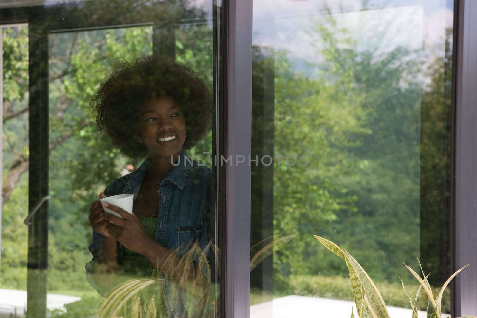 Beautiful young african american woman drinking coffee and looking through a window in her luxury home