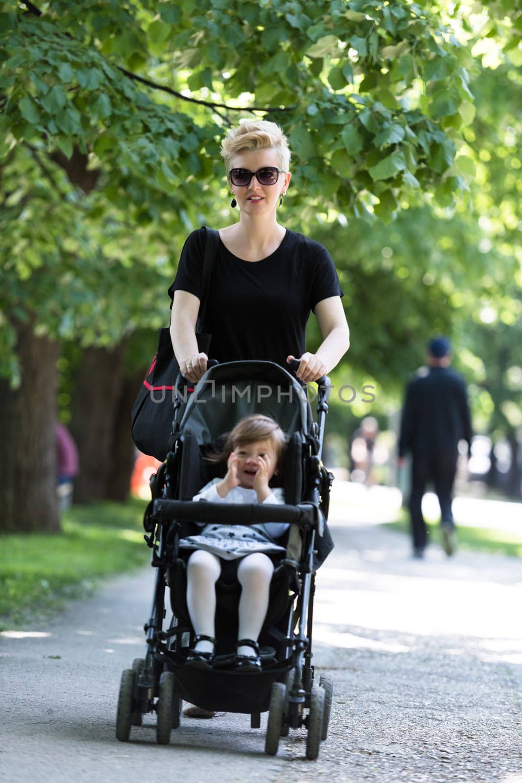 beautiful young mother with blond hair and sunglasses pushed her baby daughter in a stroller on a summer day