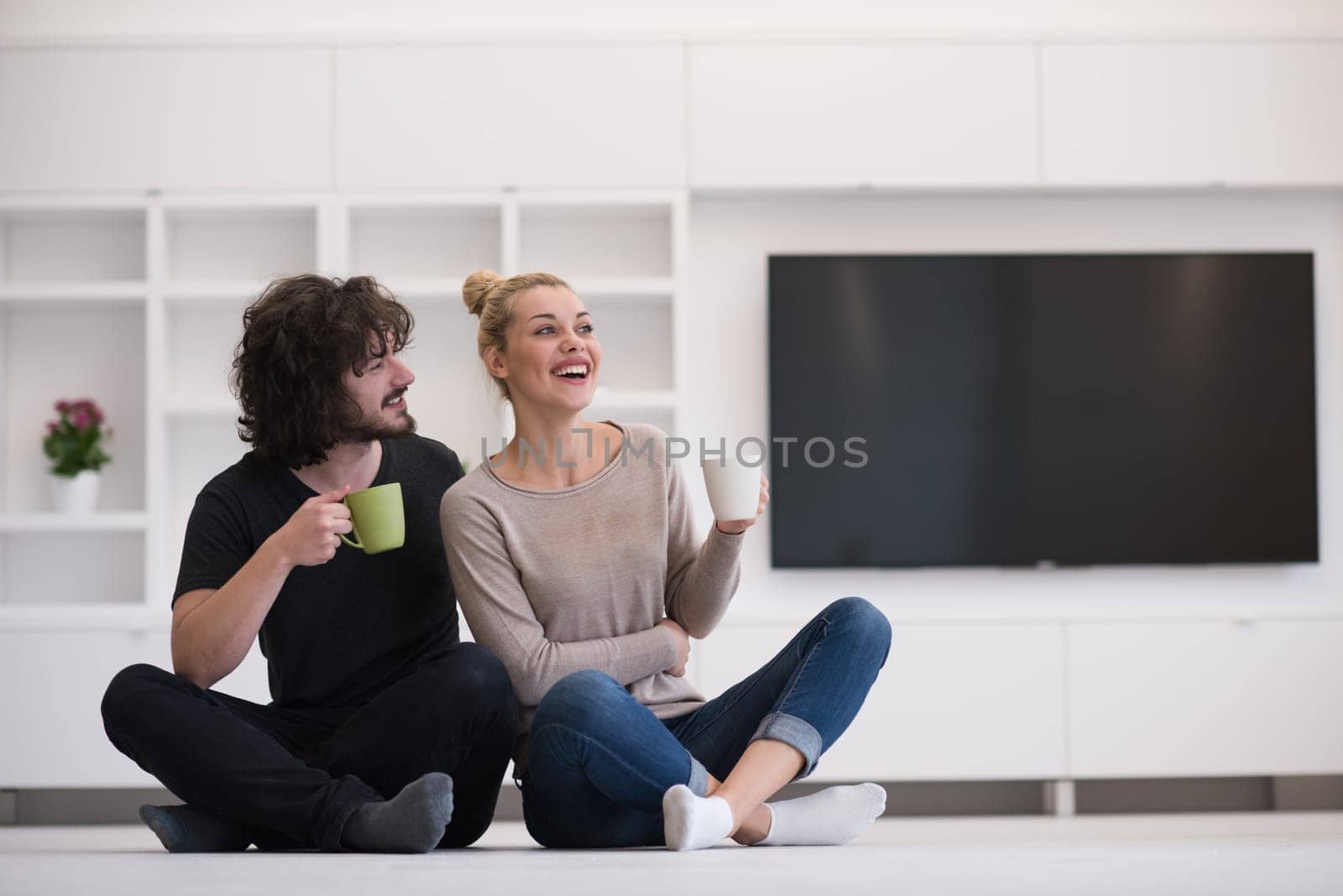portrait of young happy beautiful couple sitting on the floor and drinking coffee in their new home