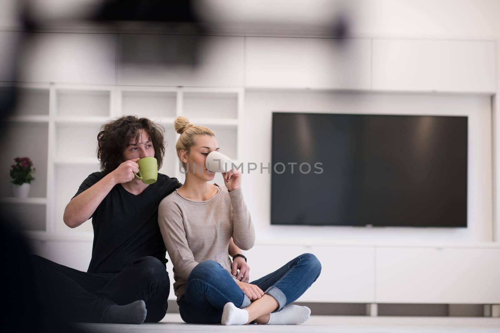 portrait of young happy beautiful couple sitting on the floor and drinking coffee in their new home