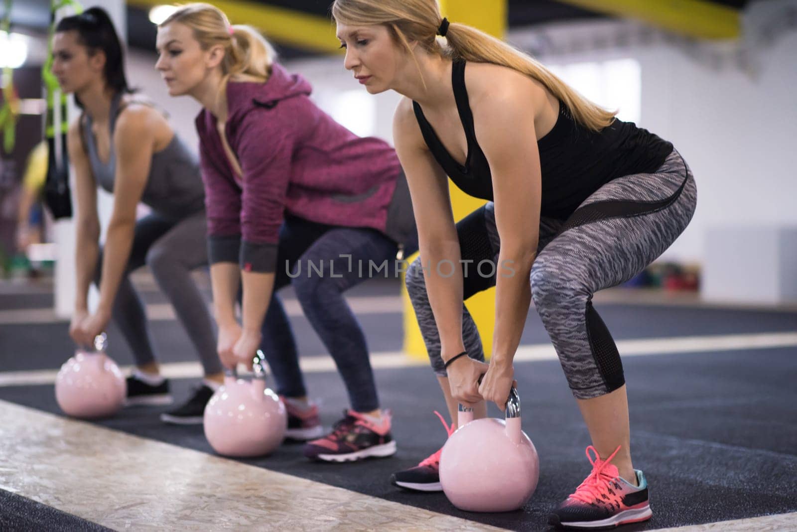 group of healthy young athletes doing exercises with kettlebells at cross fitness studio
