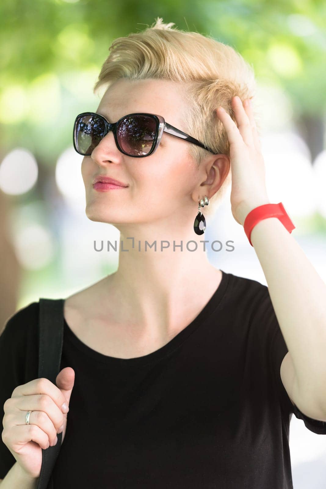 Beautiful fashionable young woman with short blond hair and sunglasses posing in the park