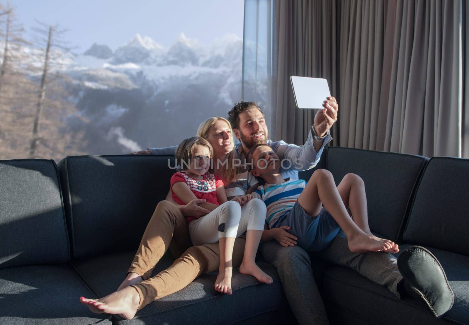 happy couple spending time with kids using tablet computer on sofa at home