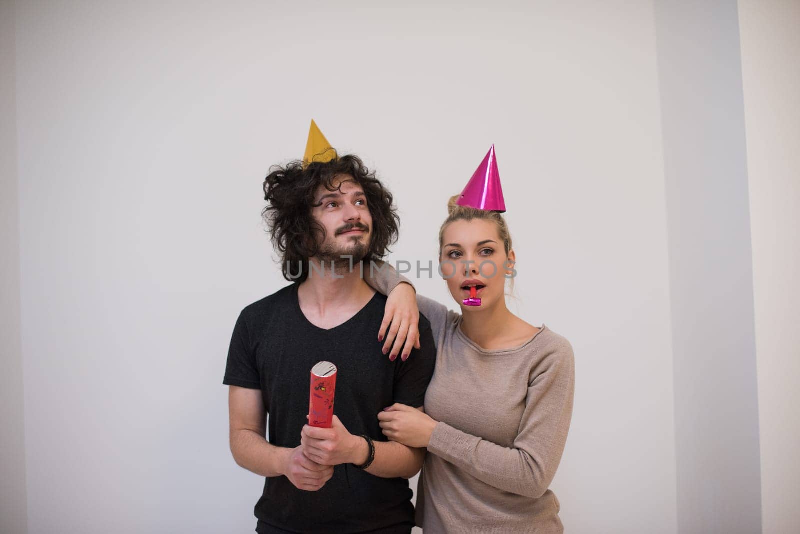 Young happy couple in party hats blowing in whistle isolated on a white background