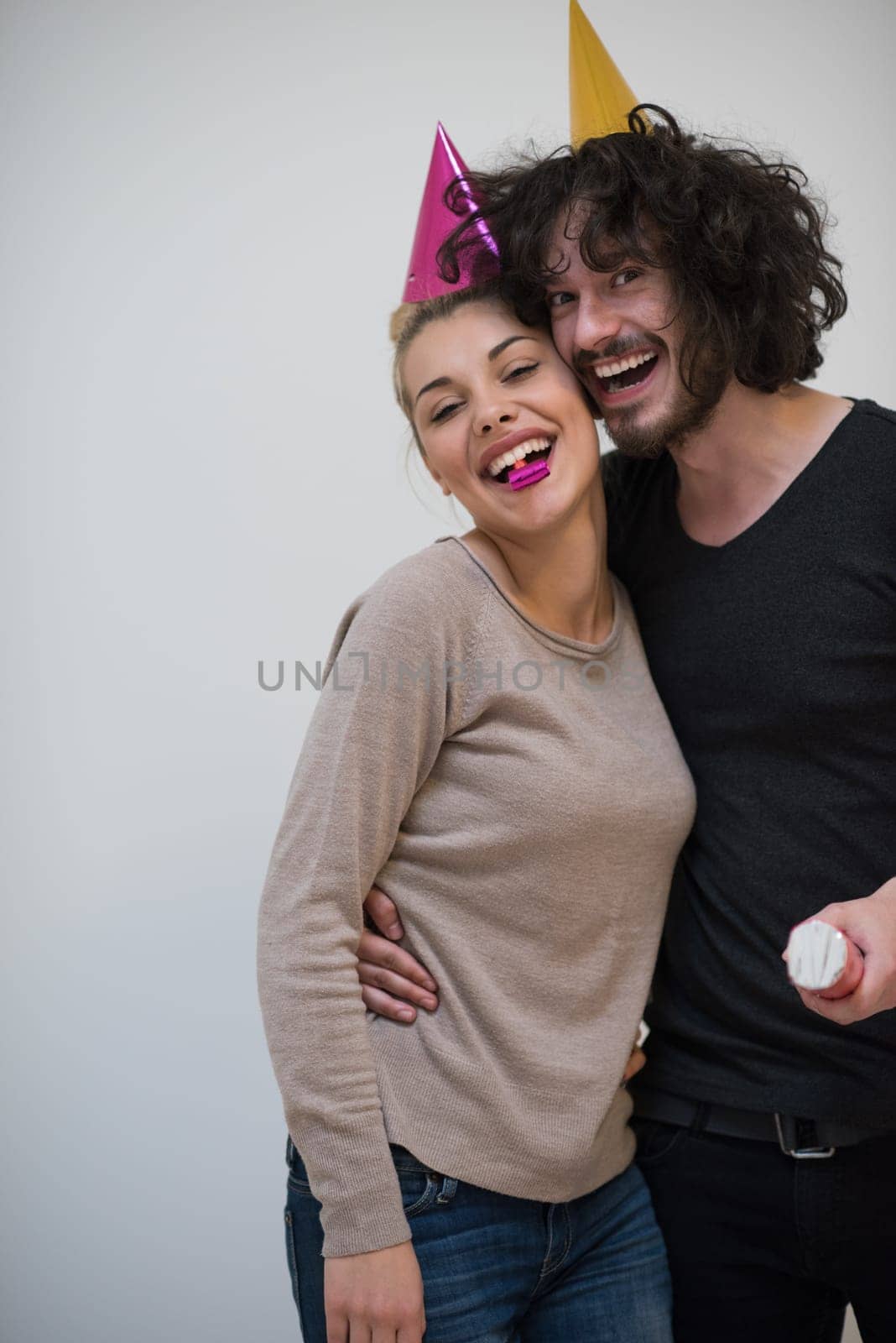 Young happy couple in party hats blowing in whistle isolated on a white background