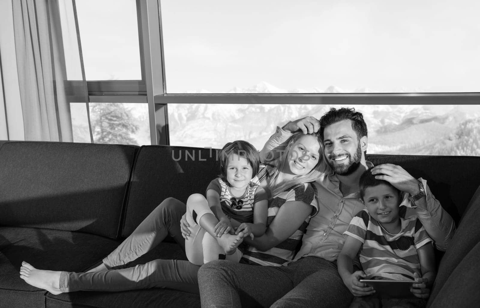 happy couple spending time with kids using tablet computer on sofa at home