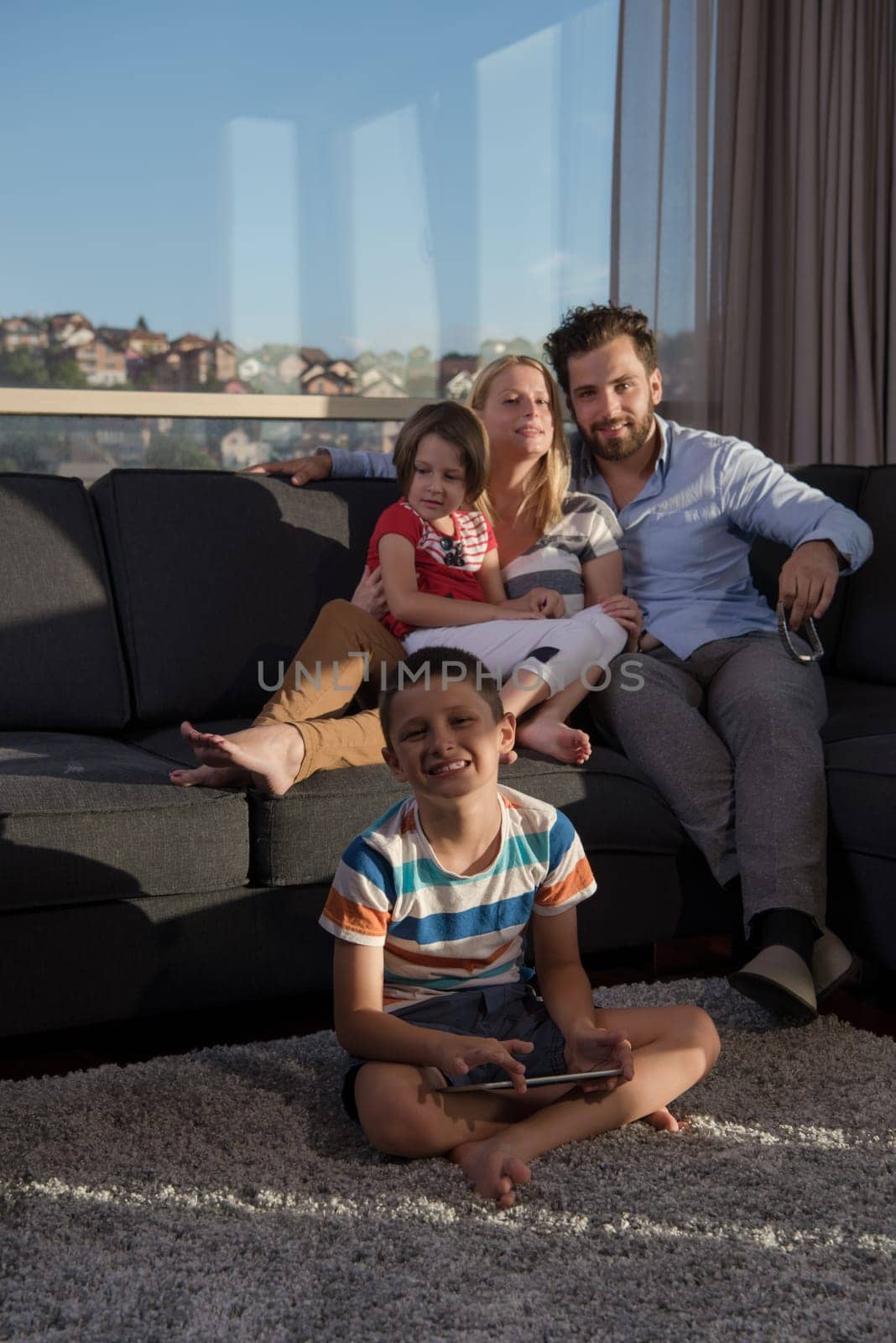 happy couple spending time with kids using tablet computer on sofa at home