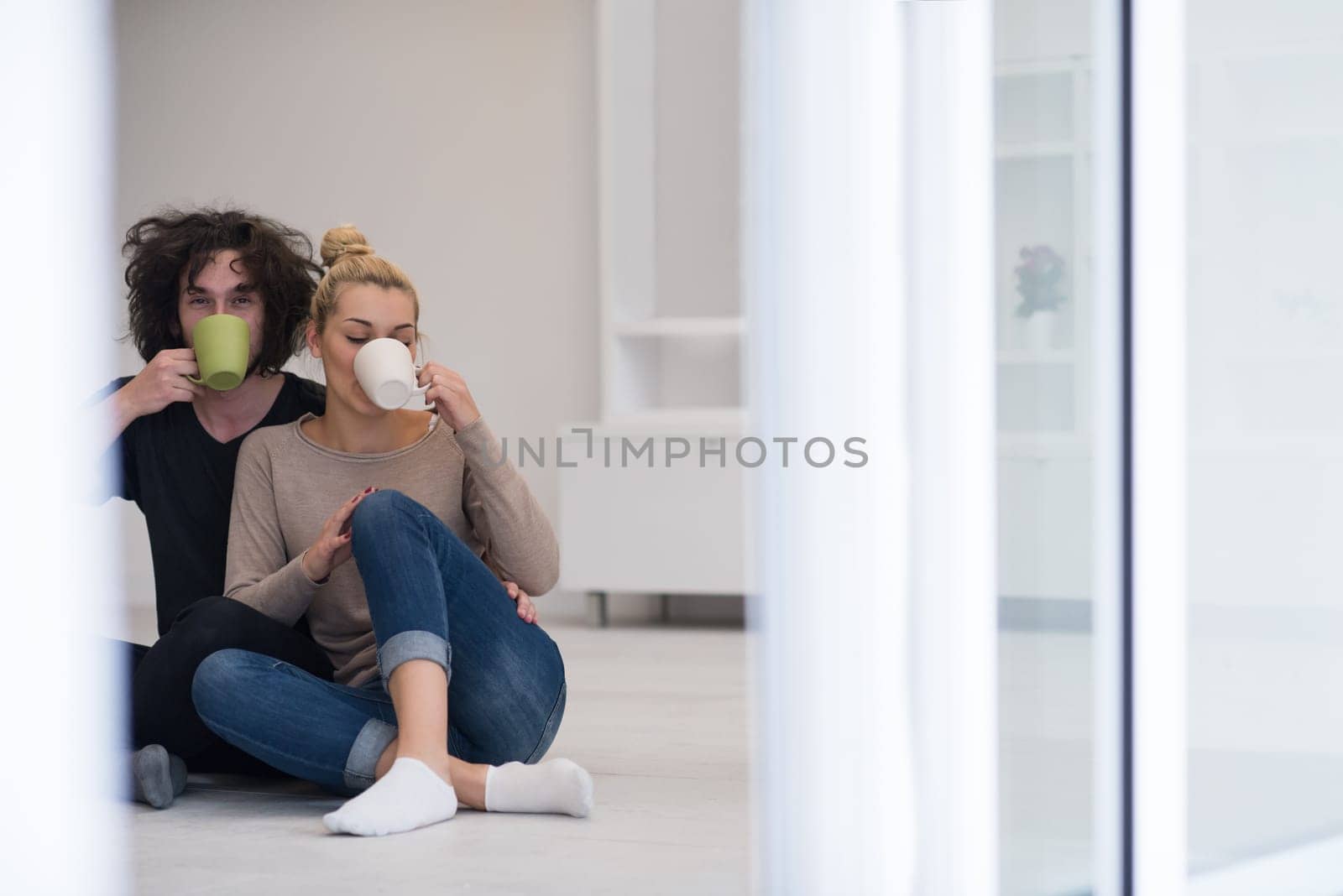 portrait of young happy beautiful couple sitting on the floor and drinking coffee in their new home