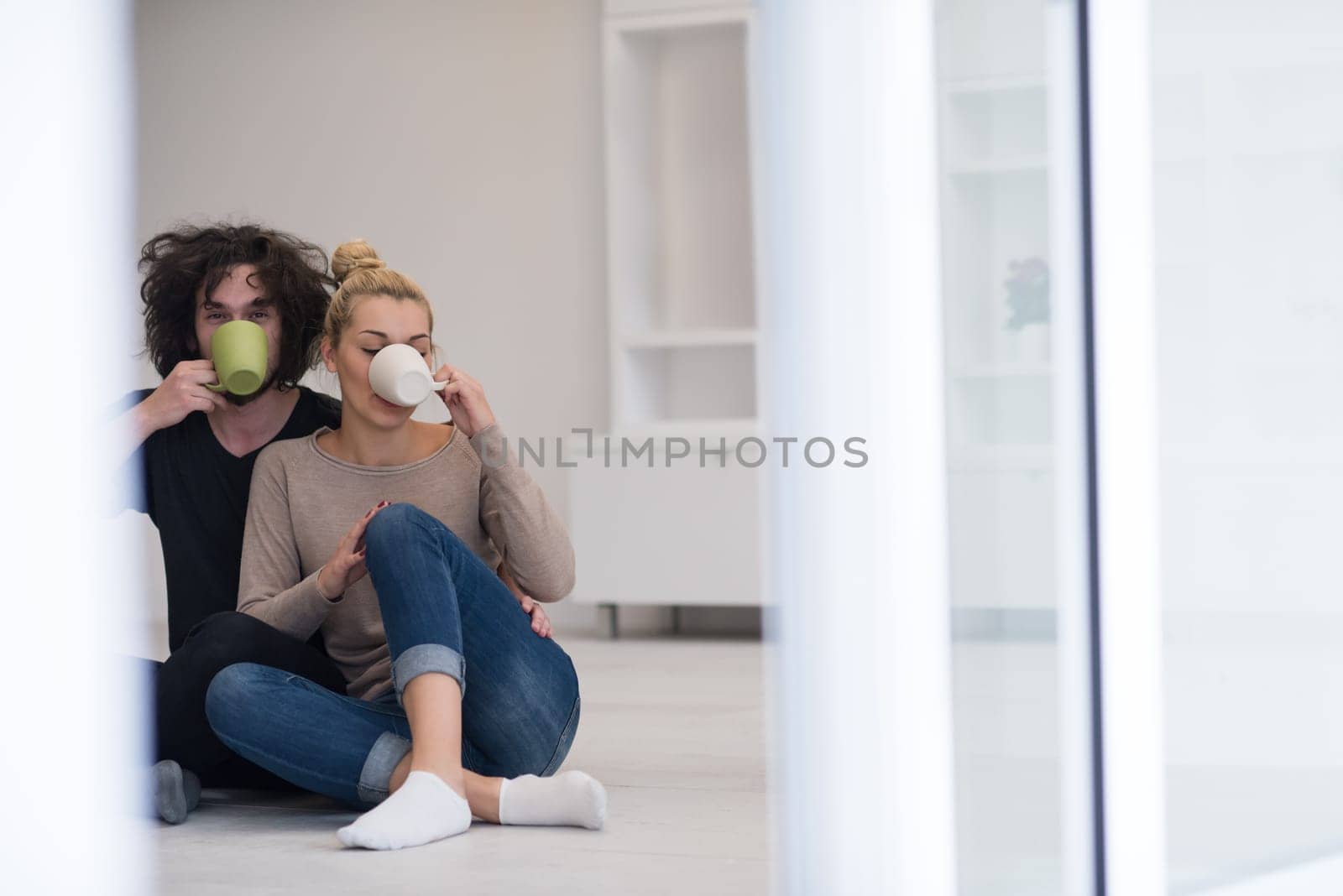 portrait of young happy beautiful couple sitting on the floor and drinking coffee in their new home