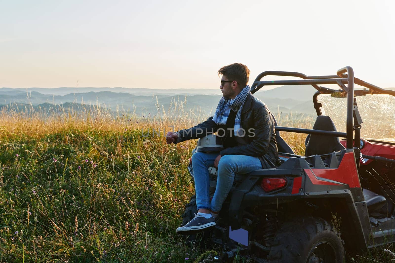 portrait of young happy excited man enjoying beautiful sunny day while driving a off road buggy car on mountain nature