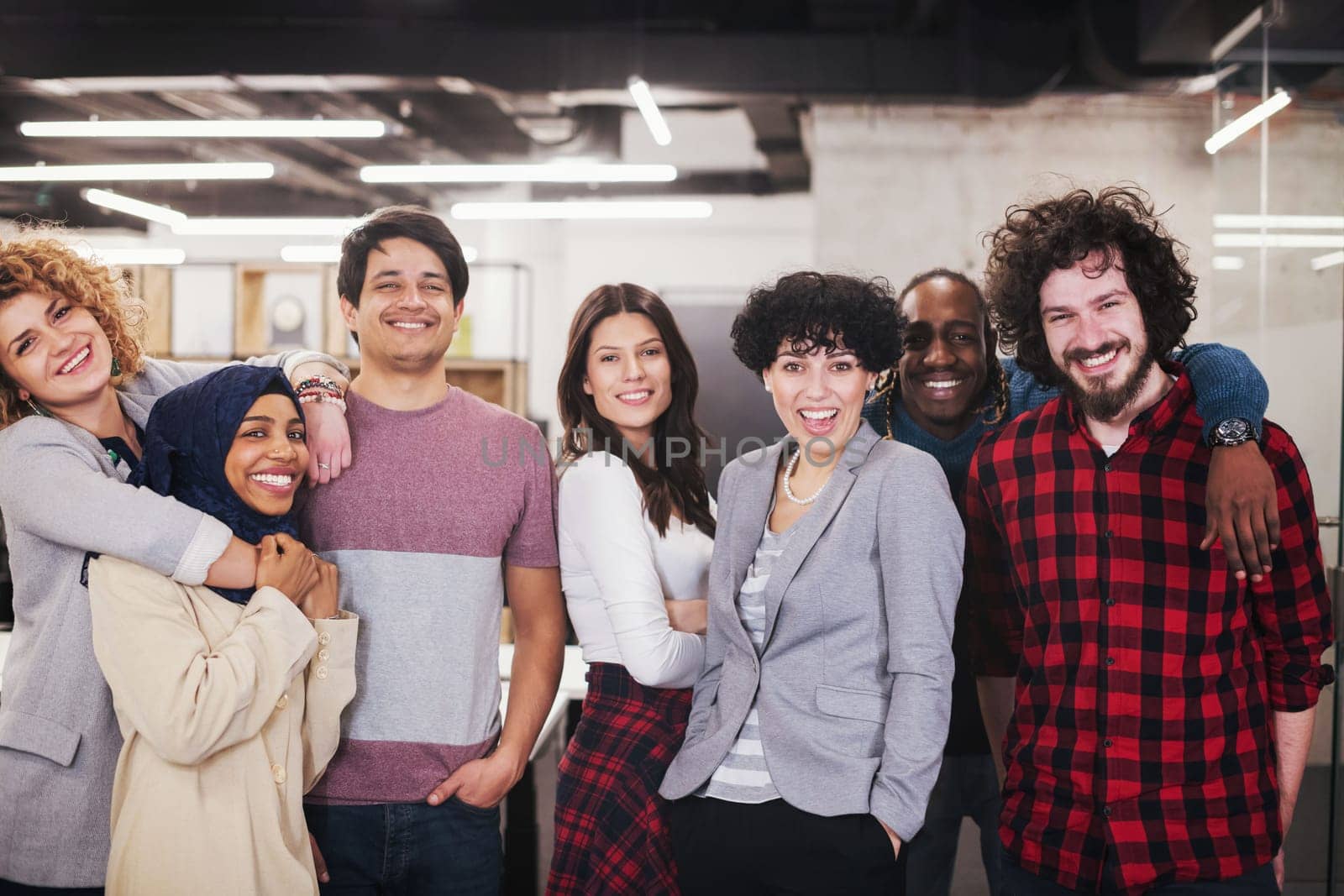 portrait of young excited multiethnics business team of software developers standing and looking at camera while celebrating success at modern startup office