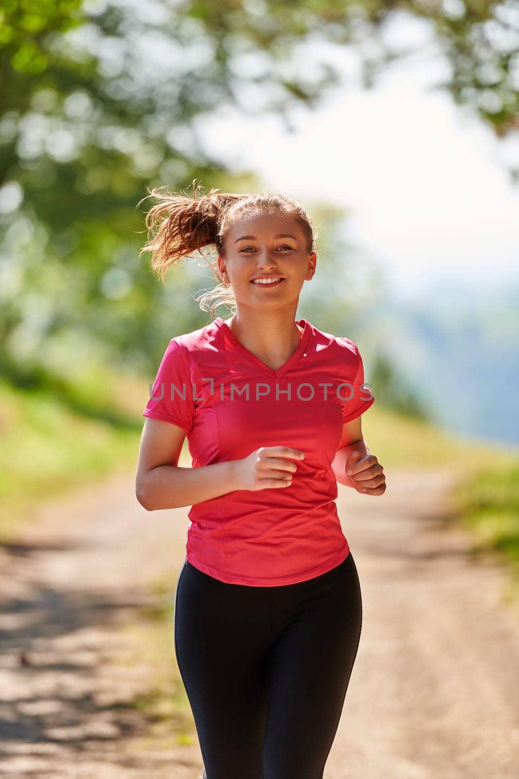 woman enjoying in a healthy lifestyle while jogging on a country road through the beautiful sunny forest, exercise and fitness concept