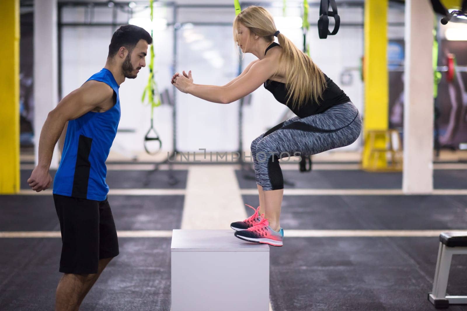 young athletic woman training with personal trainer  jumping on fit box at cross fitness gym