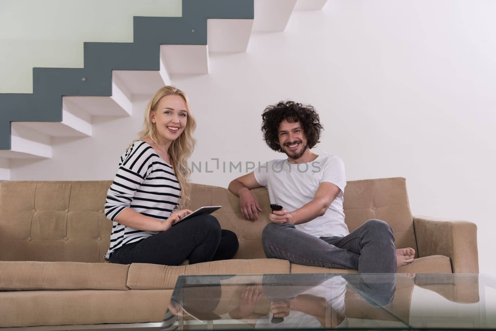 Young couple relaxes on the sofa in the luxury living room, using a tablet and remote control