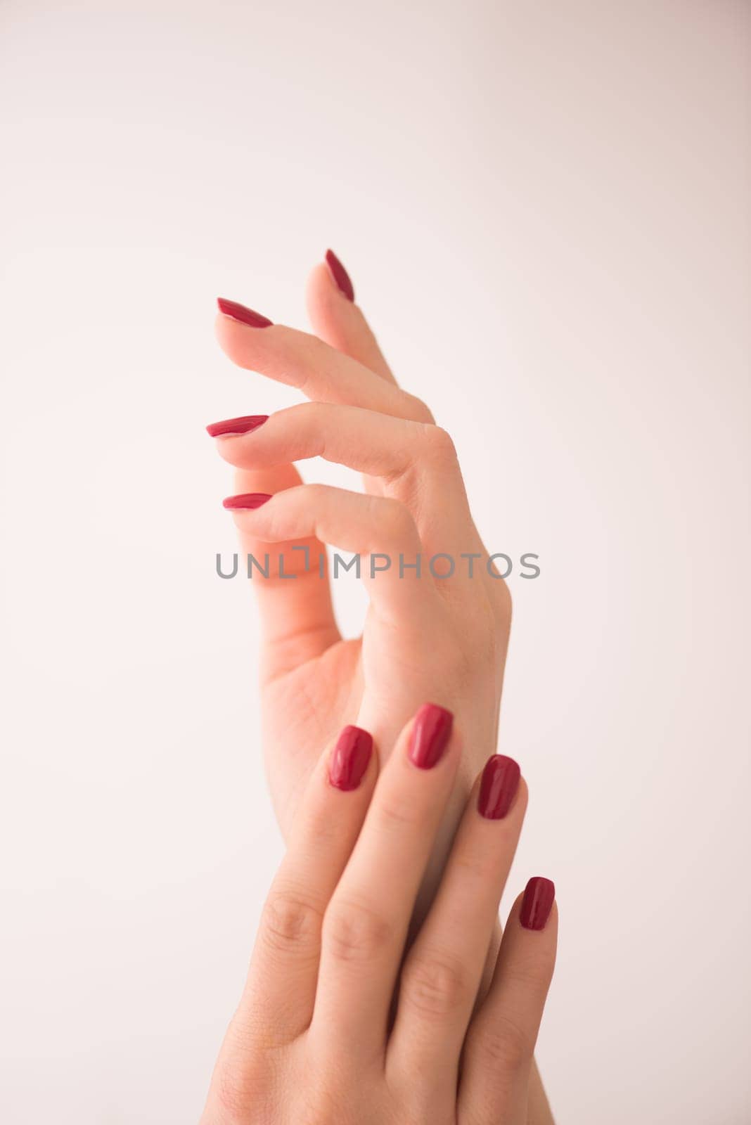 closeup of hands of a young woman with long red manicure on nails against white background