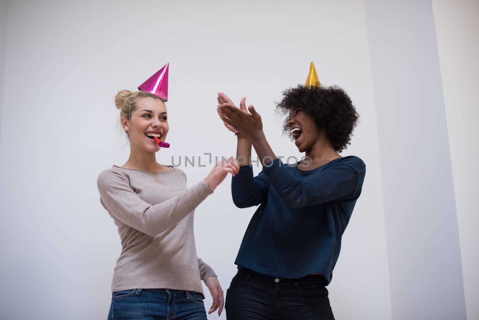 people and celebration concept  young multiethnics smiling women in party caps blowing to whistles