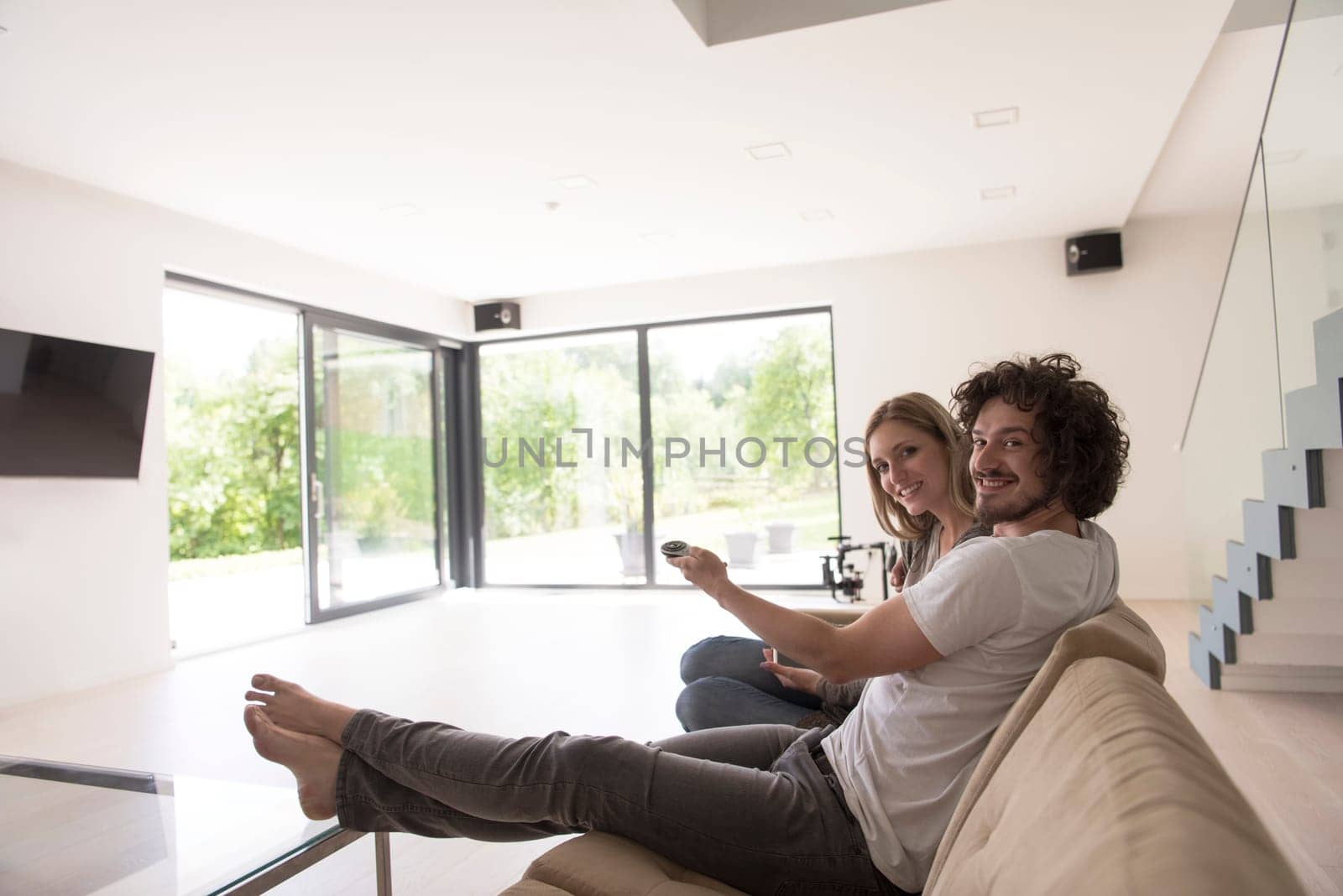 Young couple relaxes on the sofa in the luxury living room, using a tablet and remote control