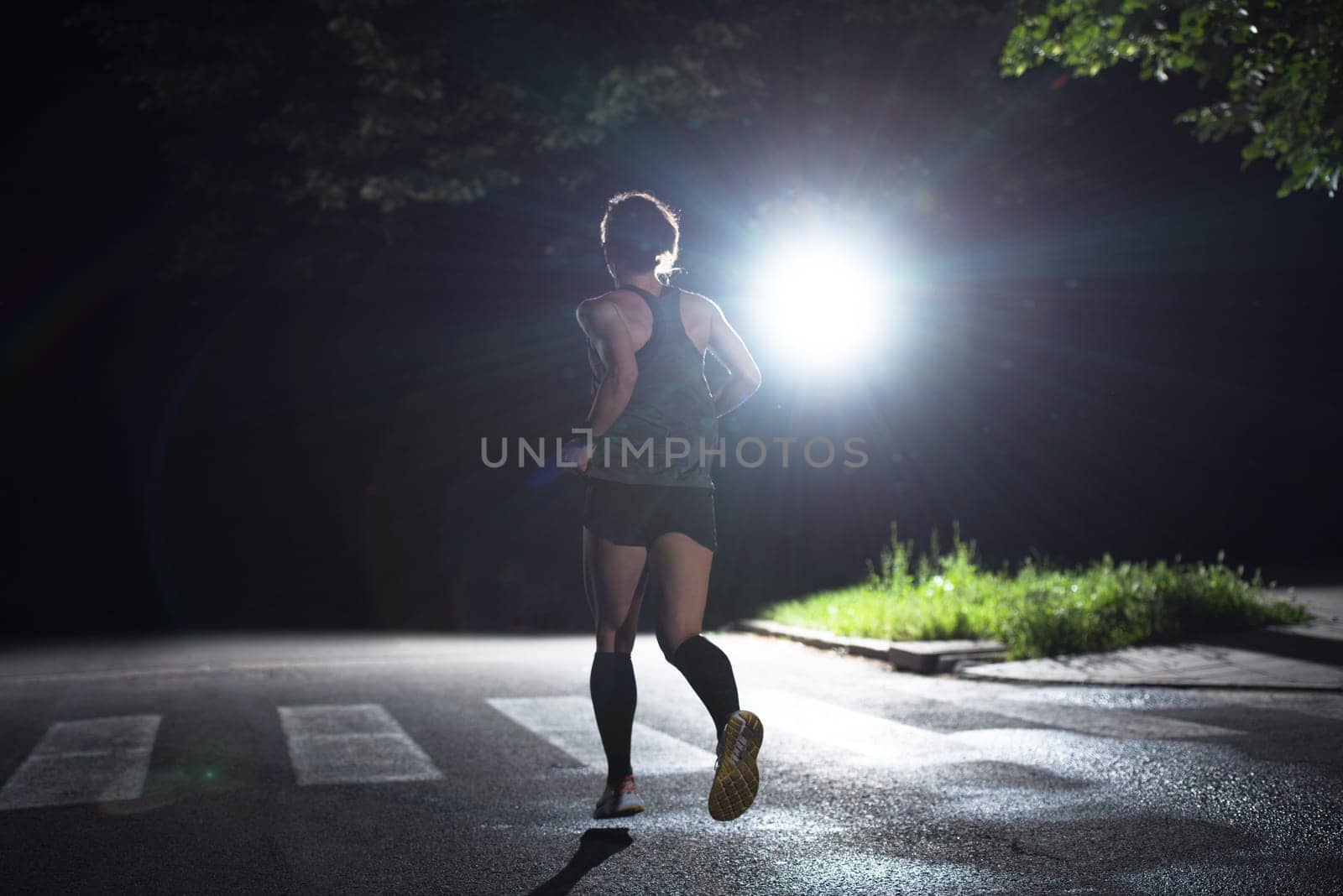 fit muscular female runner training for marathon running at night on beautiful road in nature.